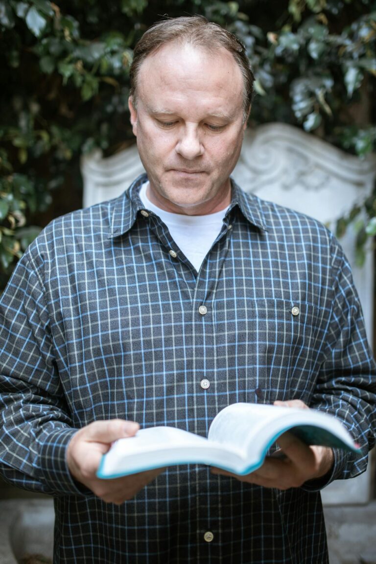 An adult man reads a Bible outdoors, exuding peace and contemplation in a serene setting.