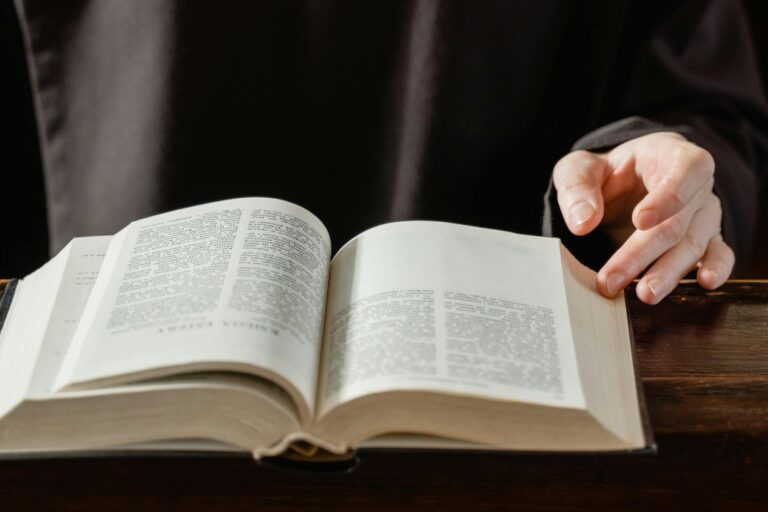 Close-up of a person turning pages of an open Bible on a wooden desk.
