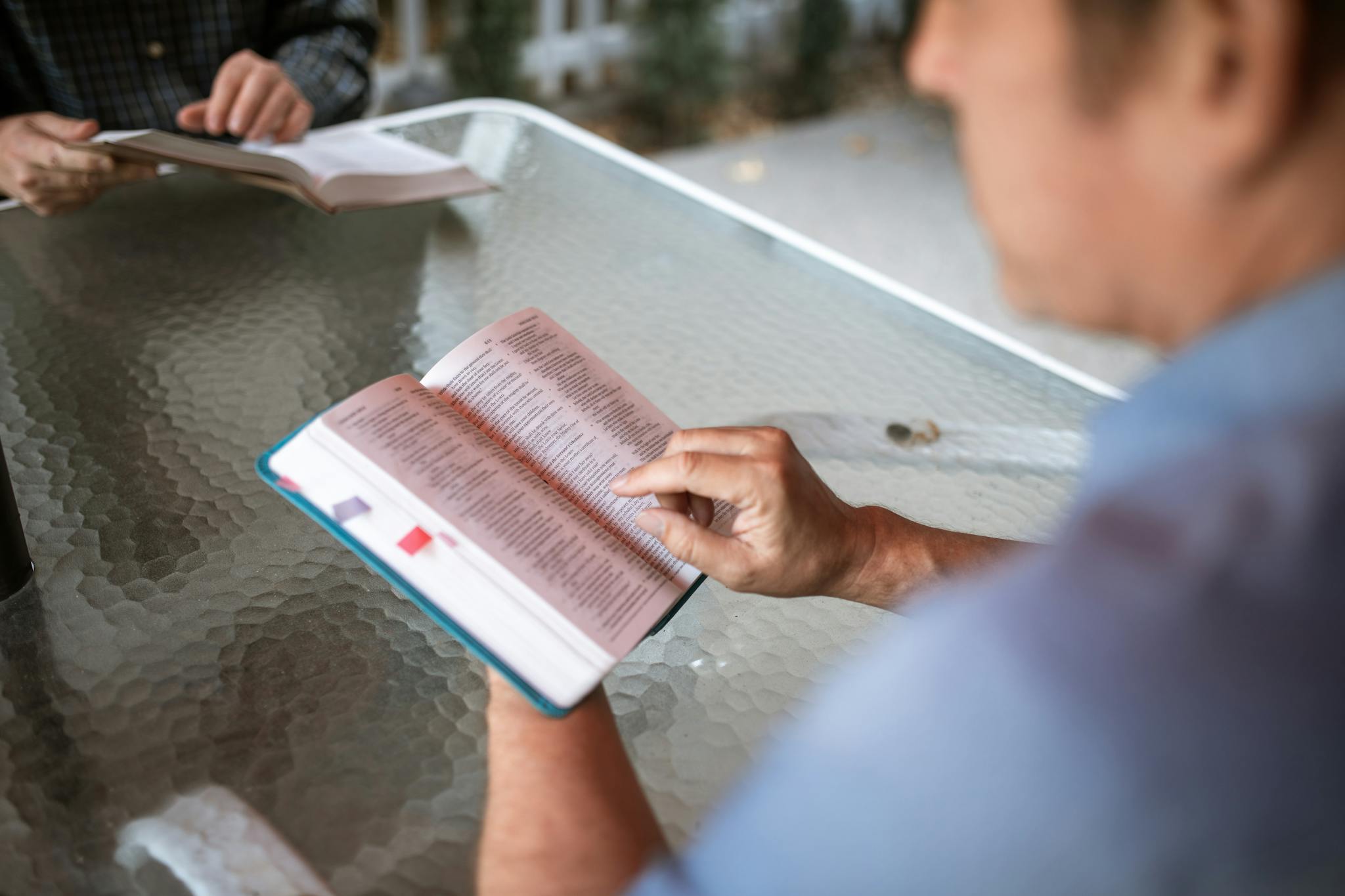 Two adults engaged in Bible study at a glass table outdoors, promoting faith and connection.